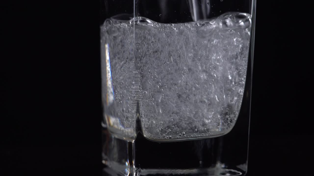 테이블 위의 유리잔에 신선한 미네랄 물을 부어, 검은색 배경에 산소 공을 가진 신선한 스파클링 음료