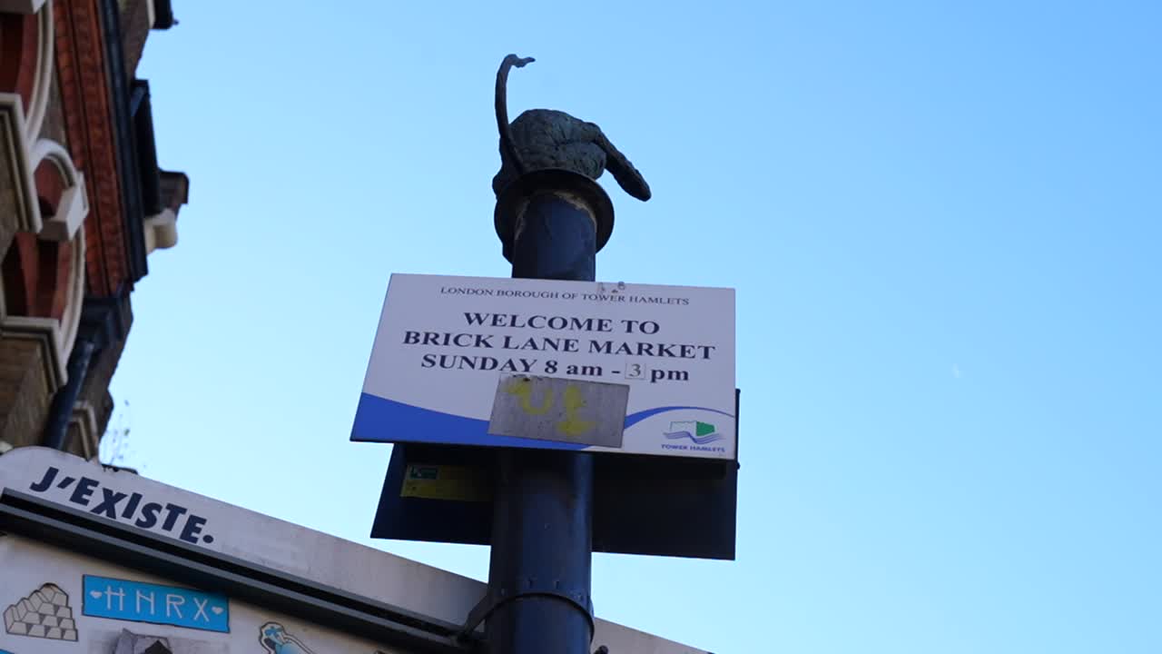 Brick Lane Market sign displaying Sunday hours with London street architecture in background