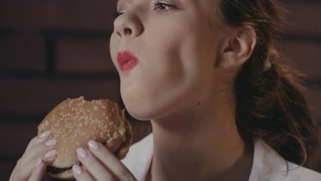 Hungry-woman-eating-burger-on-brick-wall-background-in-fast-food-cafe