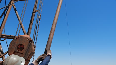 rear view of a man wearing helmet and gloves and holding a metal pipe. low angle view at the equipment at the site for oil production.