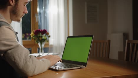 Alguien-Está-Escribiendo-En-La-Computadora-Portátil-Con-Pantalla-Verde-En-La-Sala-De-Estar,-Con-Luz-Del-Exterior