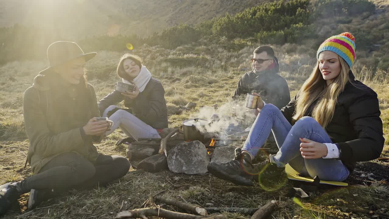 кемпинг, путешествия, туризм и люди концепция - счастливые друзья завтракают в холодное утро в горах