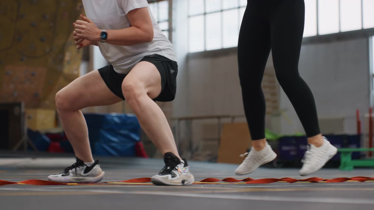 Sessione di allenamento pliometrico di badminton in coppia con affondi e squat esplosivi su campo al coperto, due atleti che eseguono esercizi sincronizzati per la parte inferiore del corpo per sviluppare potenza, stabilità e coinvolgimento del core