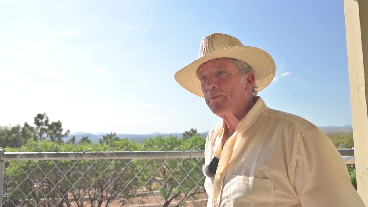 Old Man looks into distance from his patio towards orchards and mountains, then turns around and walks away, camera following.