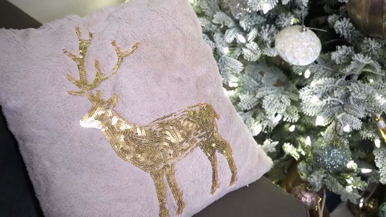 Immagine statica festiva di un cuscino natalizio con un cervo con paillettes e glitter, su uno sfondo di pini innevati.