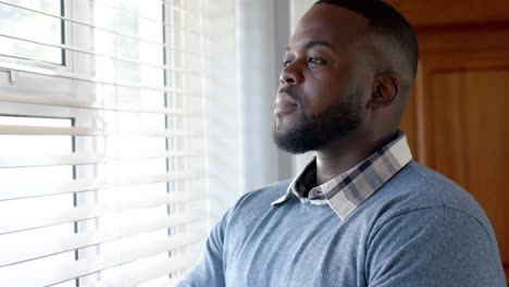 Thoughtful-african-american-man-looking-out-of-window-at-home,-in-slow-motion