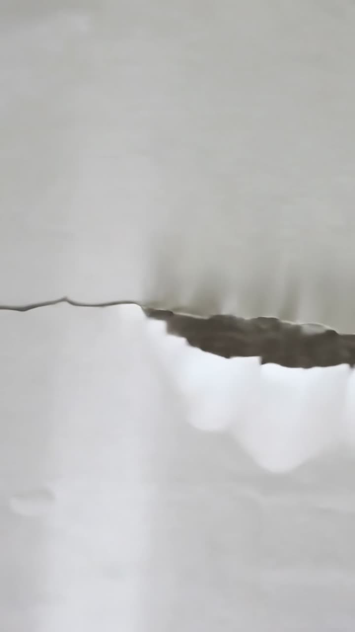 Video verticale: La telecamera panoramica lungo uno strappo in un muro bianco, che mostra il bordo arricciato e un vuoto scuro da riparare.