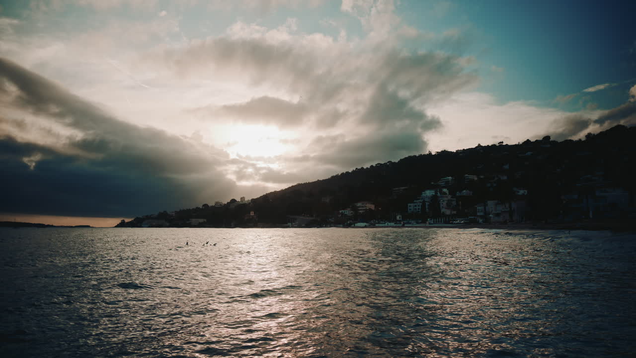 Sunset coastal view, with dramatic clouds over the hills and shimmering light on the water