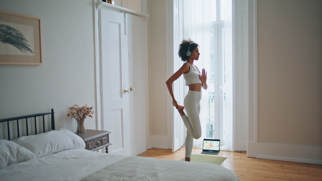 Modella che medita praticando yoga in camera da letto. Elegante signora dalla pelle scura che esegue un'asana.