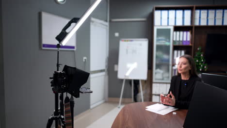 confident caucasian brunette in black jacket sits at desk in the office. law blogging concept.