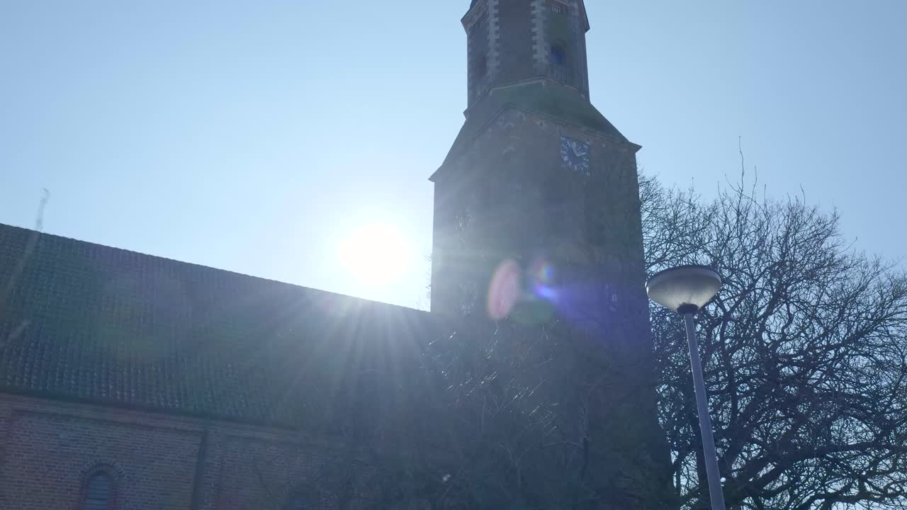 Sole splendente ed effetto lens flare dietro il campanile di una chiesa storica