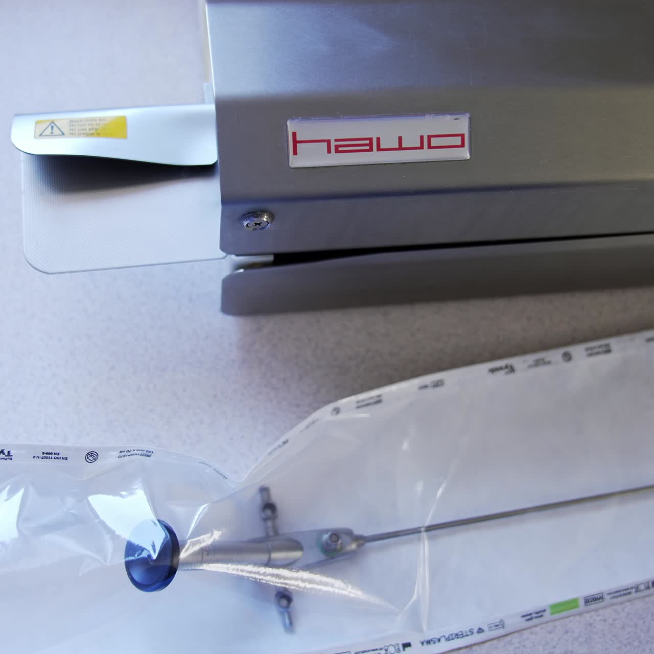 Long metal tool packed into the plastic bag in the gloved hands of medic. Nurse places the bag into equipment for sealing