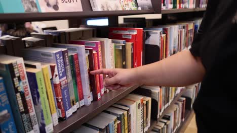 persona recogiendo un libro de la estantería de la biblioteca