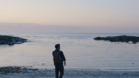 portrait of young tourist man walking on beach at sunset