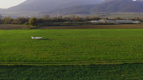 a small white aircraft taking off from grassfield with mountains backdrop in slovakia