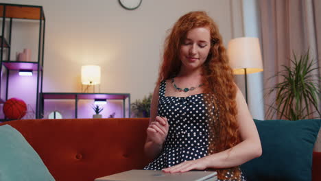 Redhead-young-woman-sitting-on-sofa-closing-laptop-pc-after-finishing-work-in-living-room-at-home