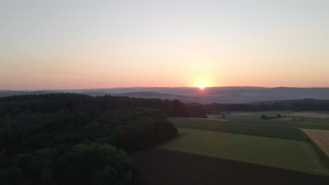 static drone footage at sunset of meadows and corn fields in a valley surrounded by forests in germany