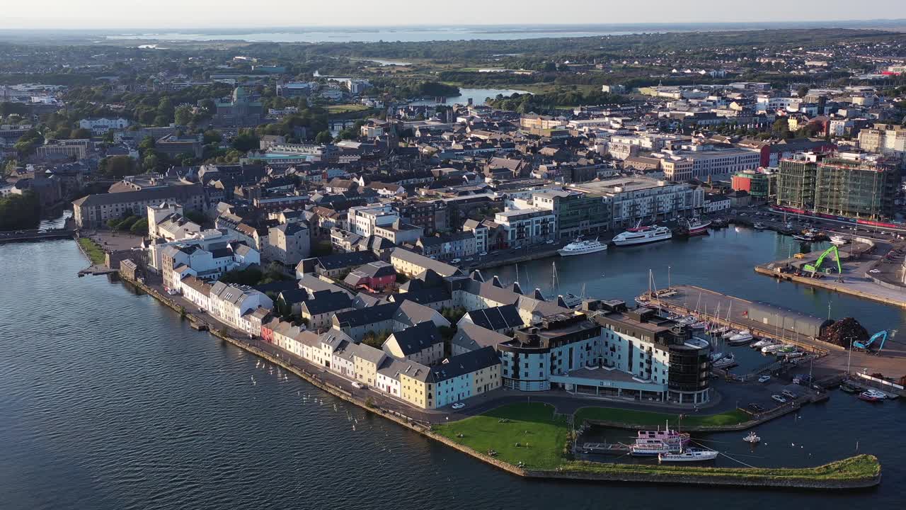 Ireland’s city of Galway in daytime as it sits by the Sea. A drone shot panning left around the dock area, showcasing the houses, busy roads and ships that are docked right beside the city.