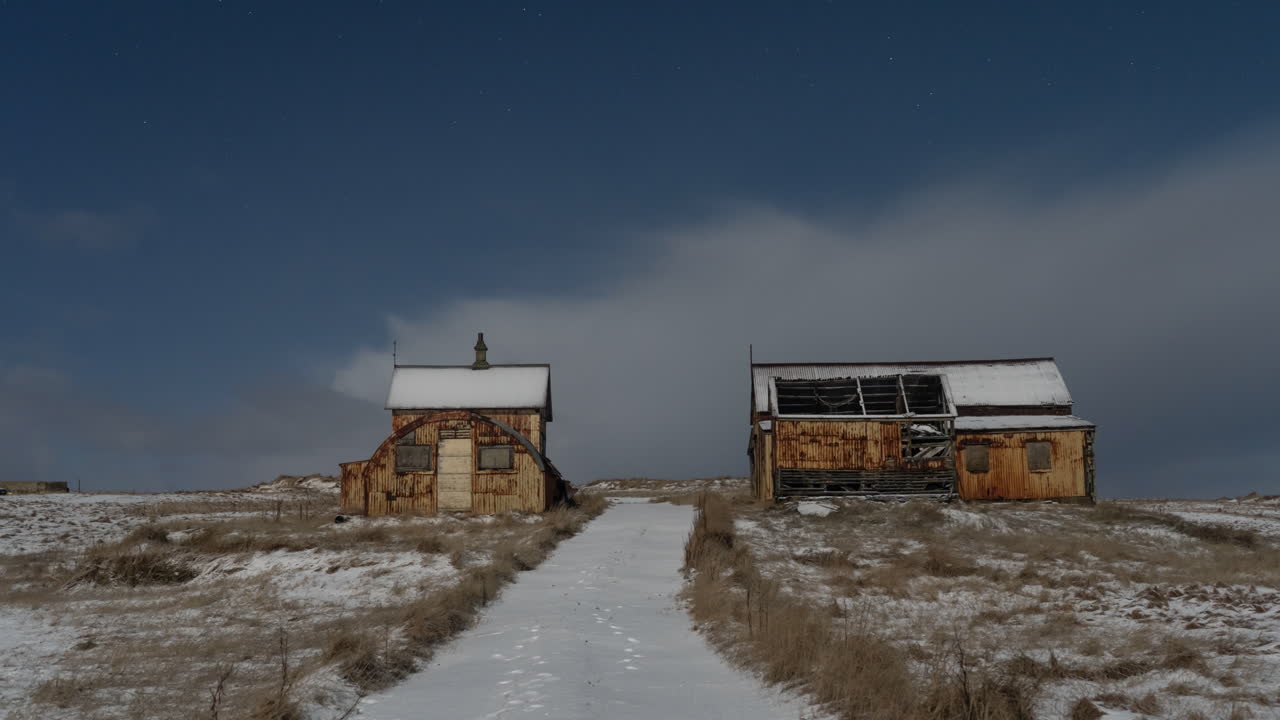 un lapso de tiempo de 12 segundos de cobertura de nubes moviéndose rápidamente sobre una granja abandonada cubierta de nieve.
