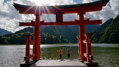 two women jumping in front of a torii gate at a japanese lake