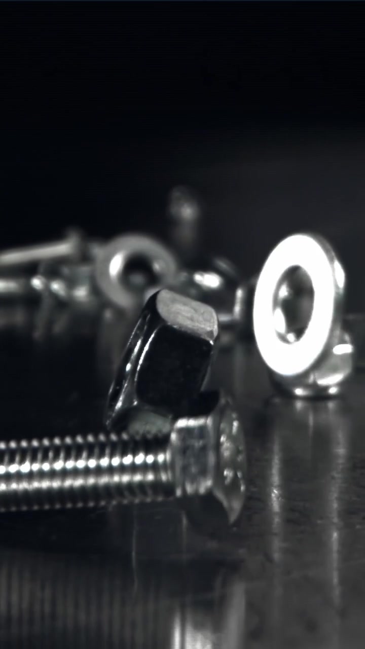 Shiny Metal Fasteners Falling onto a Dark Reflective Surface