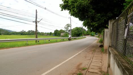 A-solo-Asian-woman-long-distance-cyclist-and-backpacker-dressed-in-athletic-clothes-riding-through-Nan-province-on-her-foldable-bicycle-on-the-left-side-of-the-road-when-a-jeep-overtakes-her,-Thailand