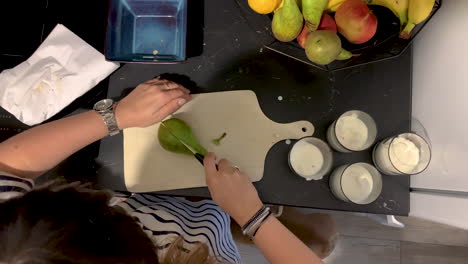 top view the girl is holding a knife in her hand and cutting a pear on a wooden board, small french bulldog go around on floor