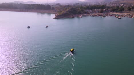 Spectacular-Aerial-view-of-boats-in-ocean-moving-towards-mountain-and-shore,-drone-shot