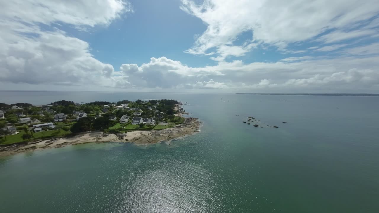 FPV drone slowly glides above sea, aerial view of coastline alongside lush green landscapes in Concarneau, Brittany, France, stunning coastal scenery.
