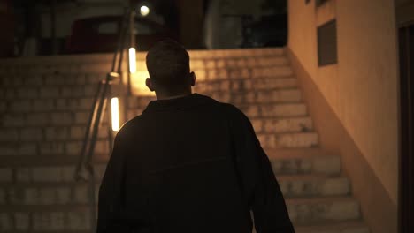 slow motion shot of man walking towards lighted stairs going up