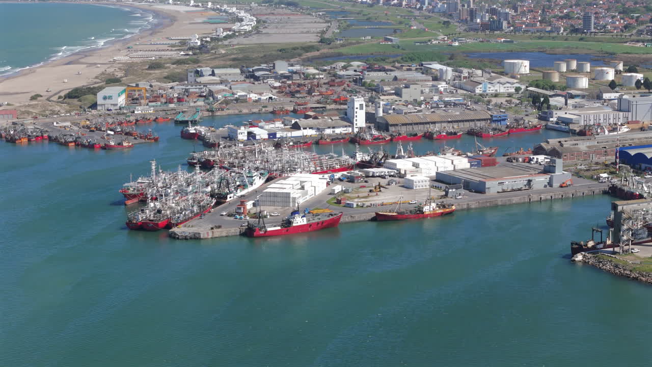 Panning aerial movement near the industrial Port of Mar del Plata area with docked cargo ships and containers along the shoreline, Argentina.