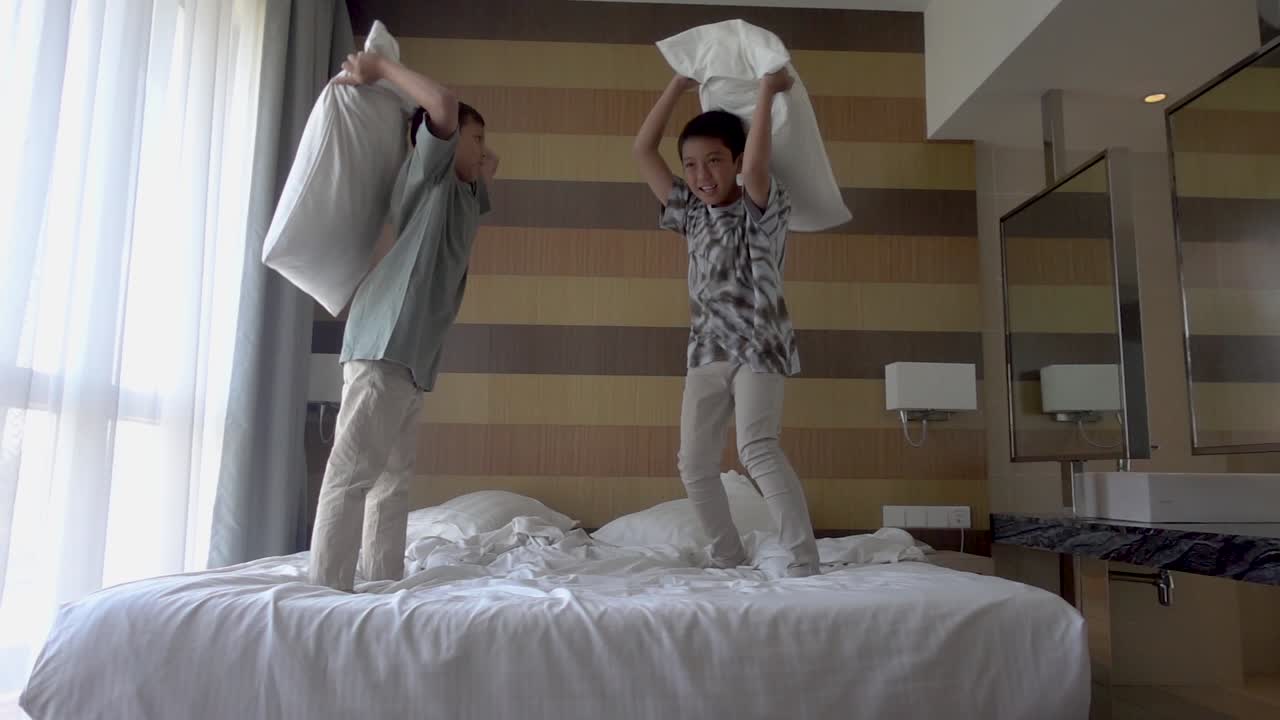 Two brothers are enjoying pillow fight on bed in apartment laughing having fun together. Leisure time, happy family and joyful people concept.