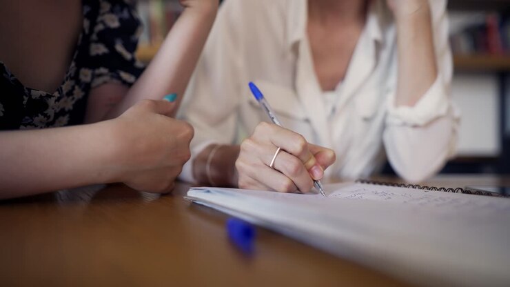 Two girls are sitting at the table and writing notea in a notebook
