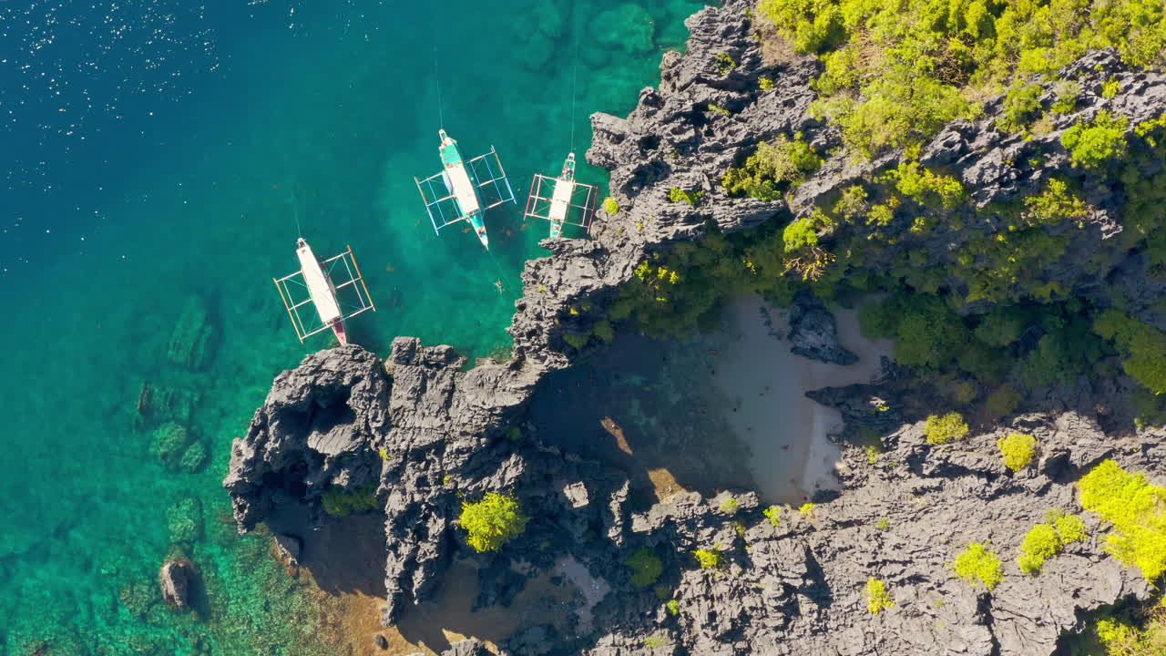 Aerial View of Tropical Paradise with Outrigger Boats, Clear Waters, and Rocky Cliffs in the Philippines