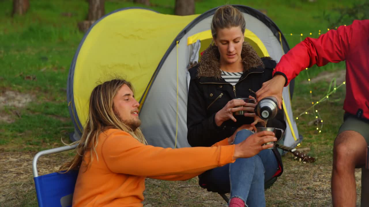 amigos tomando café cerca de la tienda de campaña en el bosque 4k