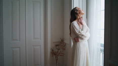 mujer joven mirando por la ventana en la mañana de casa. modelo relajado disfrutando de un fin de semana tranquilo