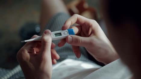 Woman-checking-and-measuring-her-temperature-with-an-axillary-thermometer-at-her-house,-above-the-shoulder-shot