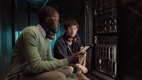 two colleagues checking work of rack server cabinet