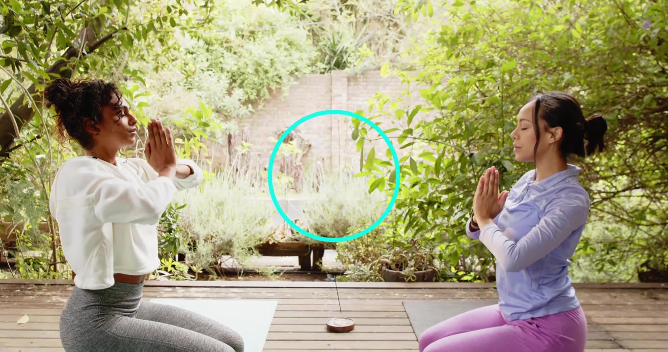Duas mulheres inspirando em tapetes de yoga, levantando os braços acima da cabeça e torcendo em um deck de madeira para bem-estar
