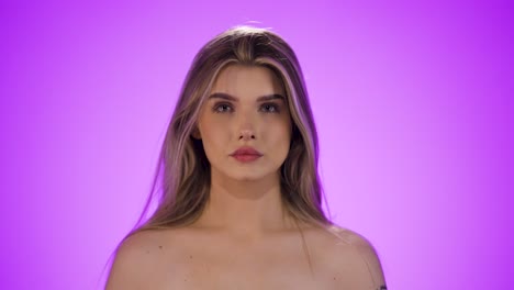 disparo medio de una joven mujer bonita revolviendo a través de su cabello antes de prepararse para salir delante del fondo púrpura en cámara lenta