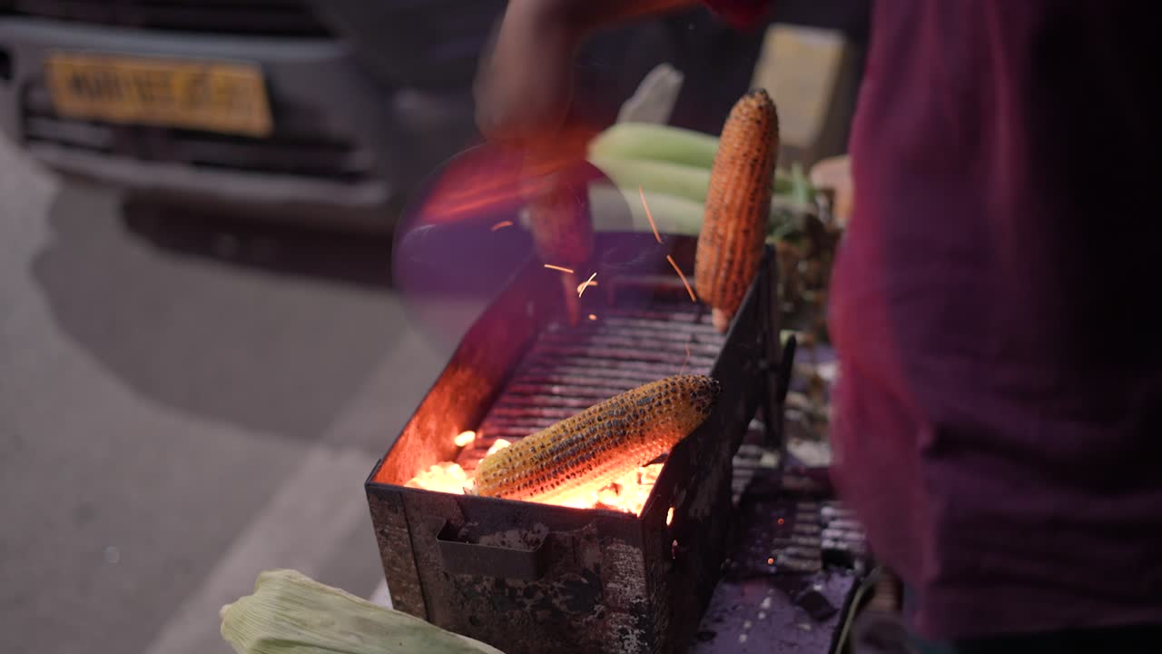 Indian vendor roasting corn on an open flame at a roadside stall