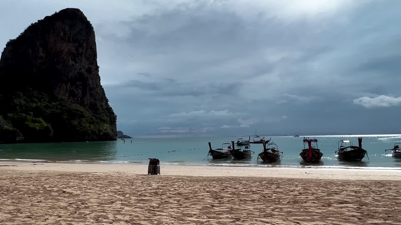 Uomo torna a prendere i bagagli sulla spiaggia con le barche a coda lunga sull'isola di Koh Phi Phi, Thailandia