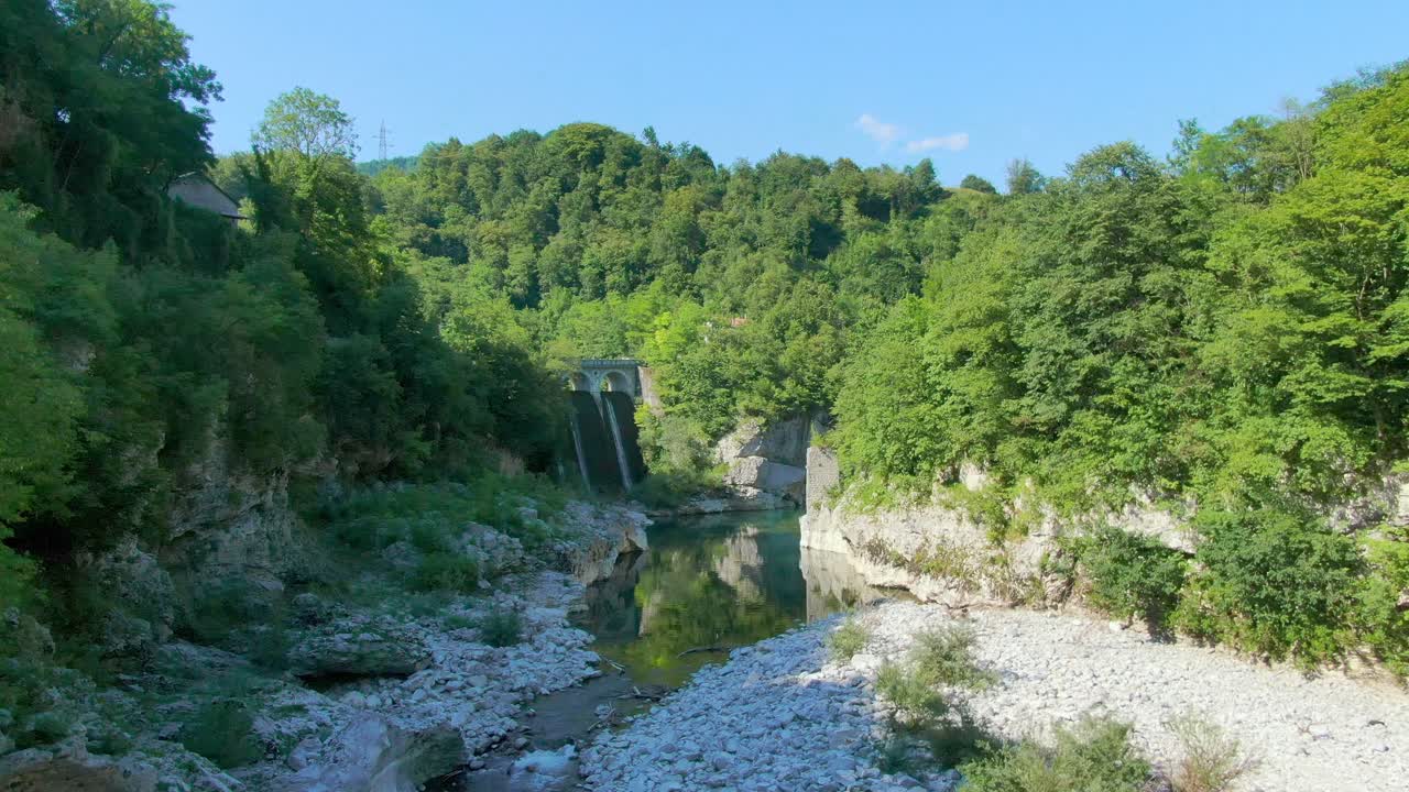 An offbeat destination with drone flying low, over a water stream amidst dense green rocky hills.Tourist destination