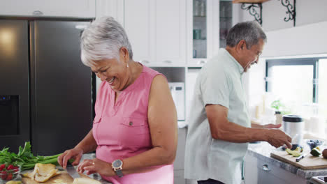 Happy-senior-biracial-couple-preparing-healthy-drink-in-kitchen