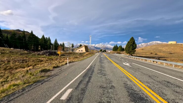 A fast-moving hyperlapse captures a scenic autumn drive along a rural highway near Lake Tekapo, with mountains, open fields, and dynamic daylight