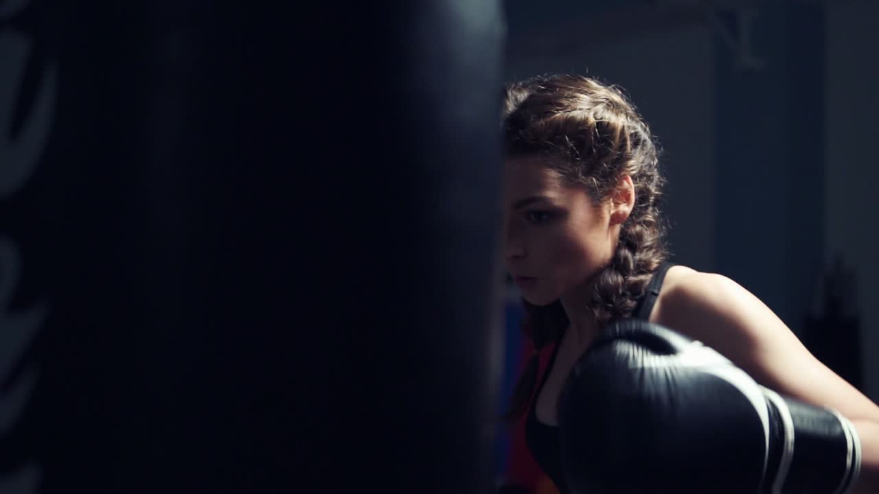 Beautiful tanned woman punching bag in fitness studio. Boxing in Slow Motion