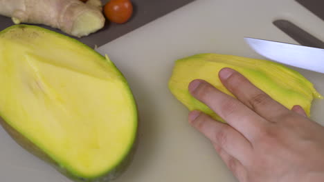 slicing nutritious ripe mango with a sharp knife in the kitchen - closeup shot