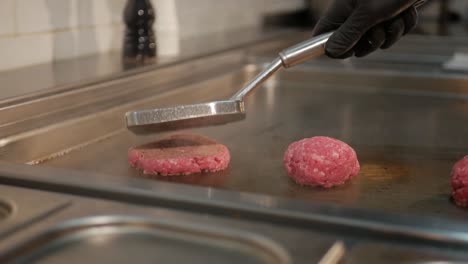 chef puts three balls of minced meat on hot stove and pushes into patties, static shot