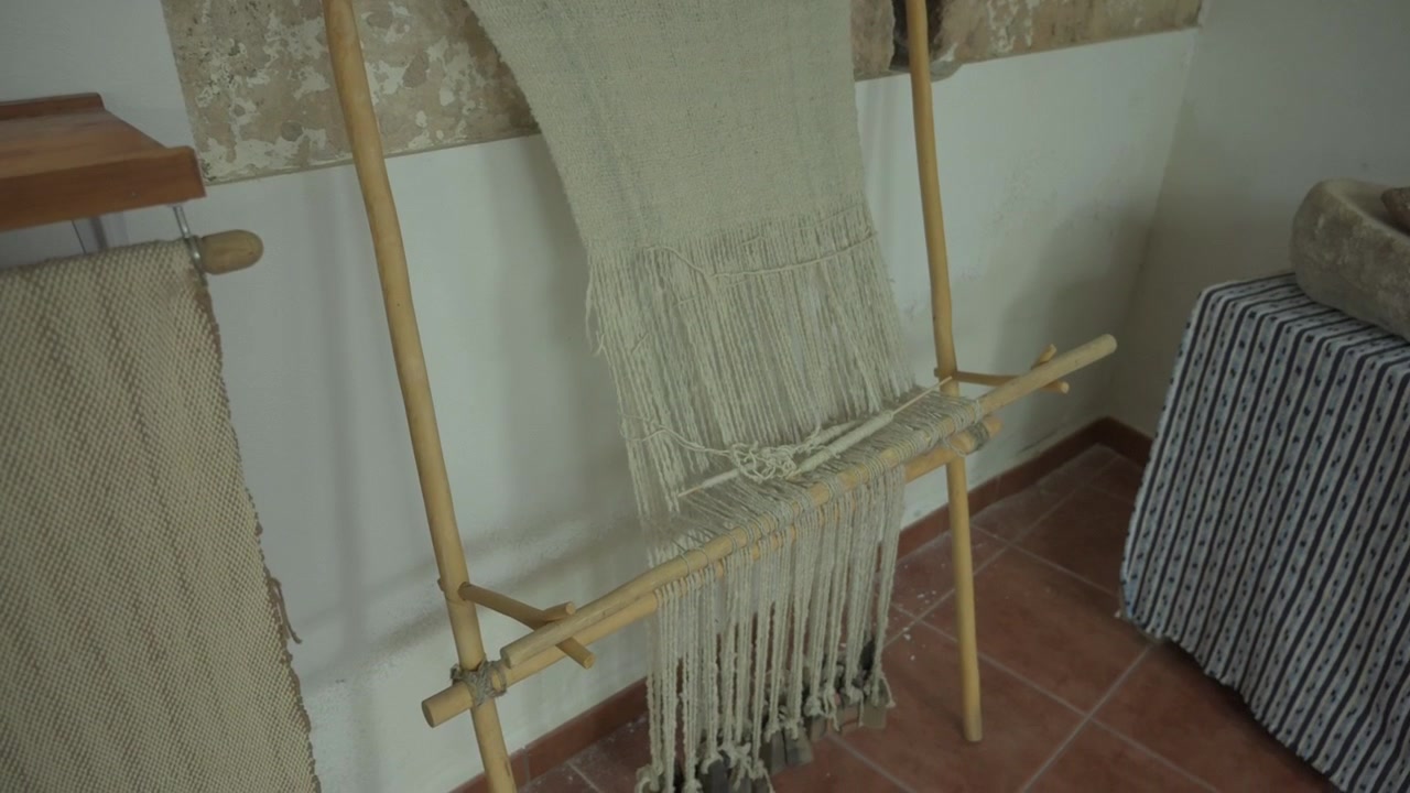 Vista statica di un telaio verticale rustico in legno a pesi con fili di fibra naturale.