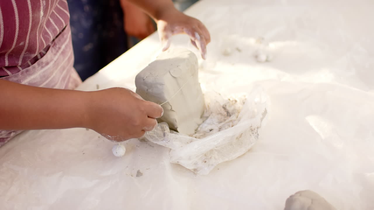 Hands of african american female potter cutting clay with wire in pottery studio, slow motion